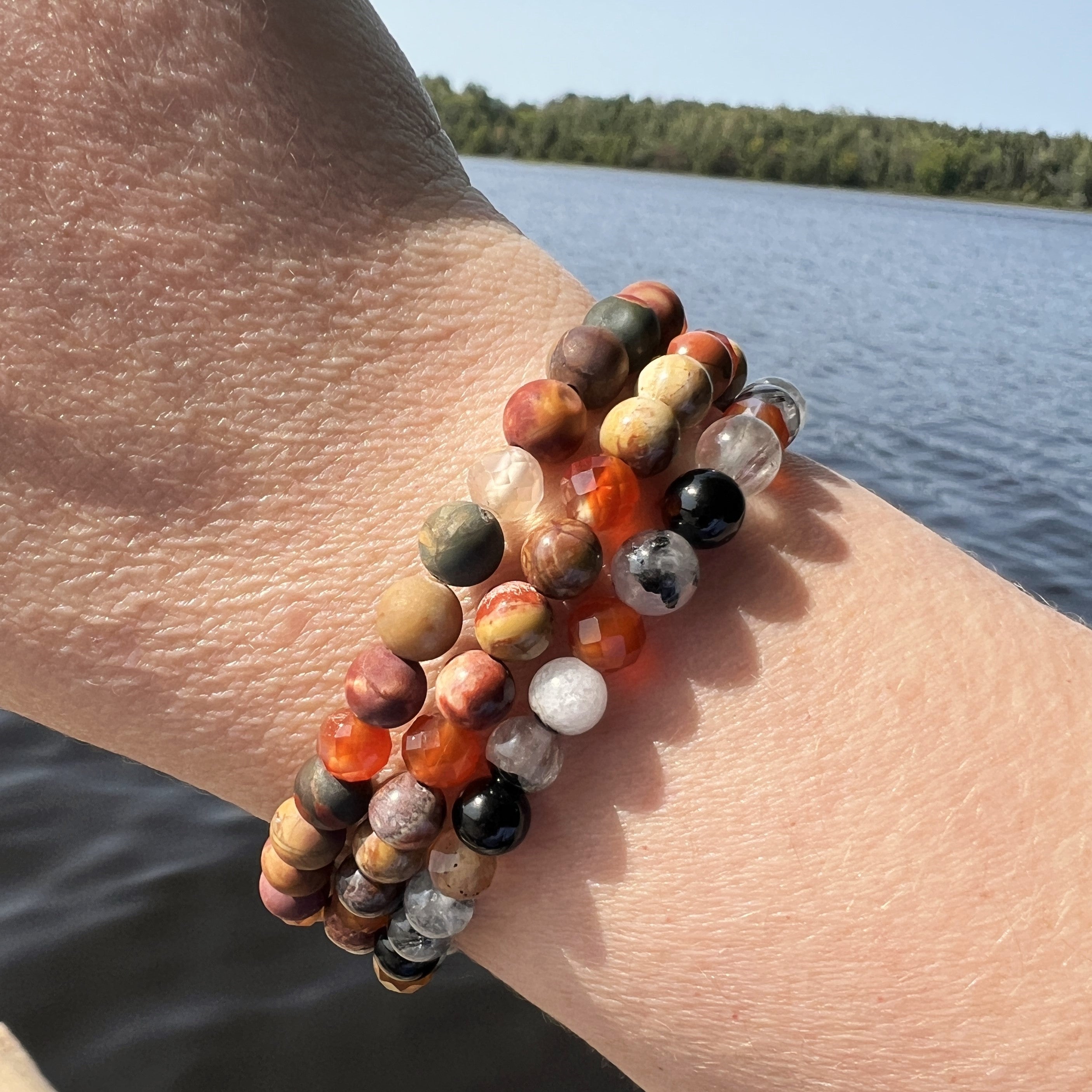 Photo showing 3 fall collection bracelets on a wrist with a water and tree background.