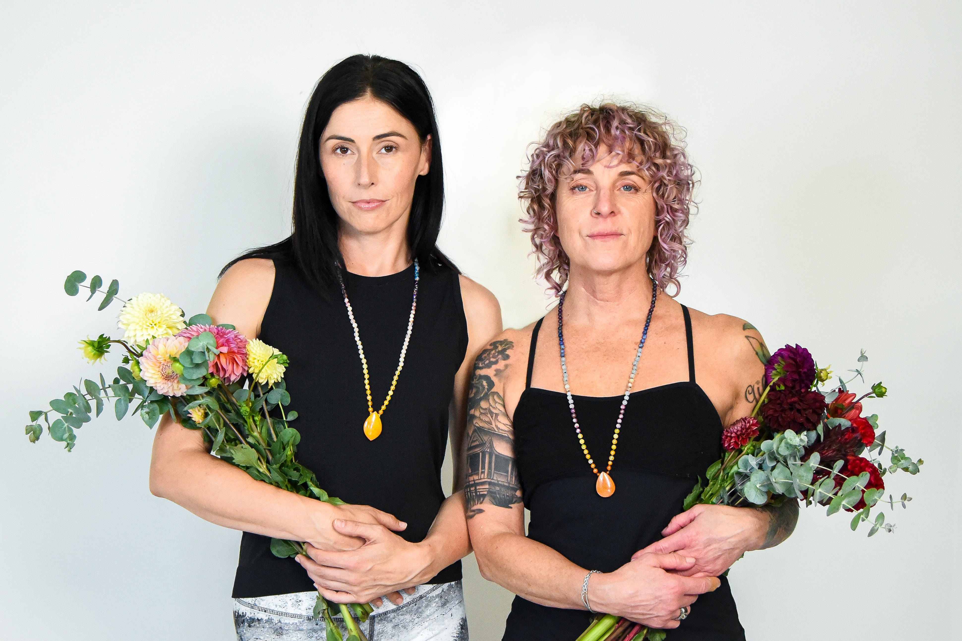 Models wearing the Sunrise and Sunset Intention Necklaces and holding flower bouquets.